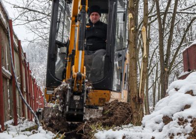 Excavator digging trench for installation on a snow-covered meadow