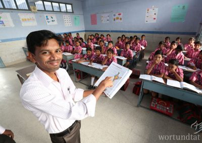 Teacher stands in front of his class holding up a geography textbook