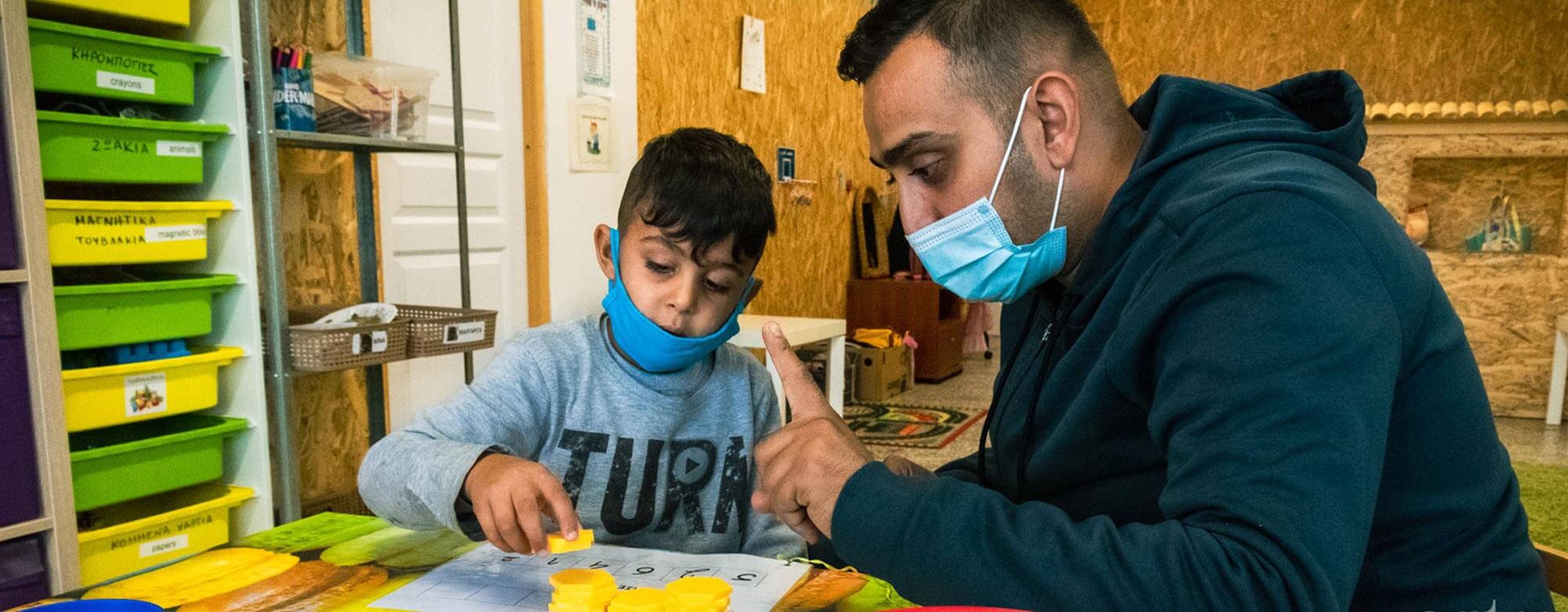 Mann zeigt Roma-Jungen, wie er mit Plättchen richtig zählen lernt.