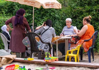 Women sitting at an outdoor table next to a sandbox - helping in Germany