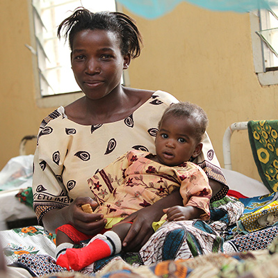 Frau mit Säugling sitzt auf einem Krankenhausbett