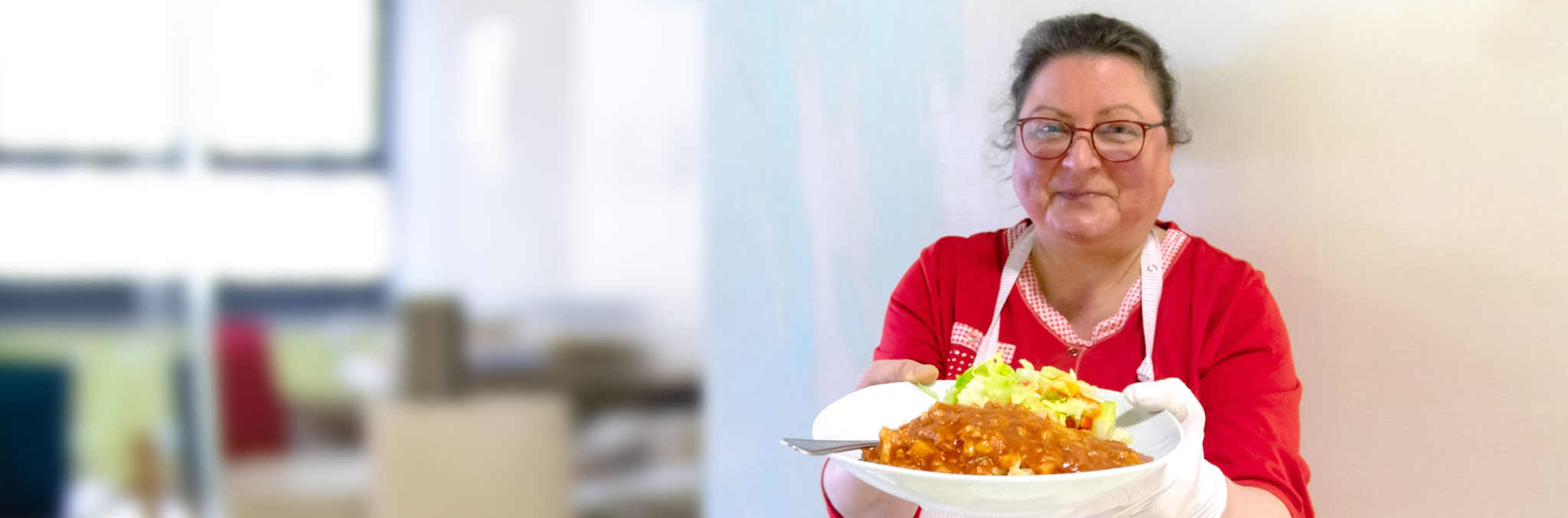 Teller mit Essen - Schale mit Salat - im Hintergrund die Köchin