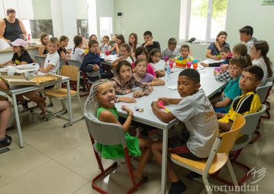 Kinder zwischen 5 und 12 Jahren sitzen eng gedrängt zusammen an Tischen und warten aufs Essen