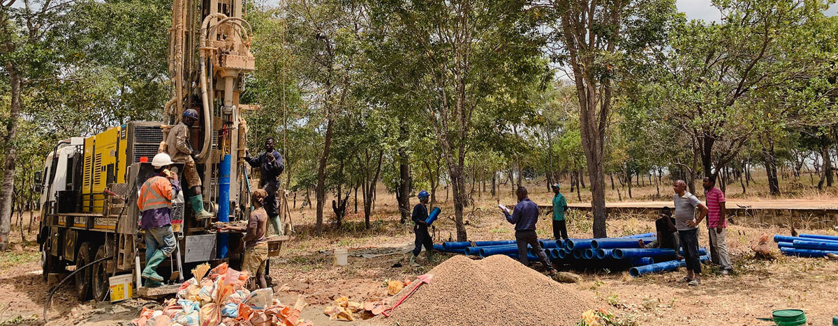 A machine for drilling wells, workers, blue plastic pipes inserted into the borehole